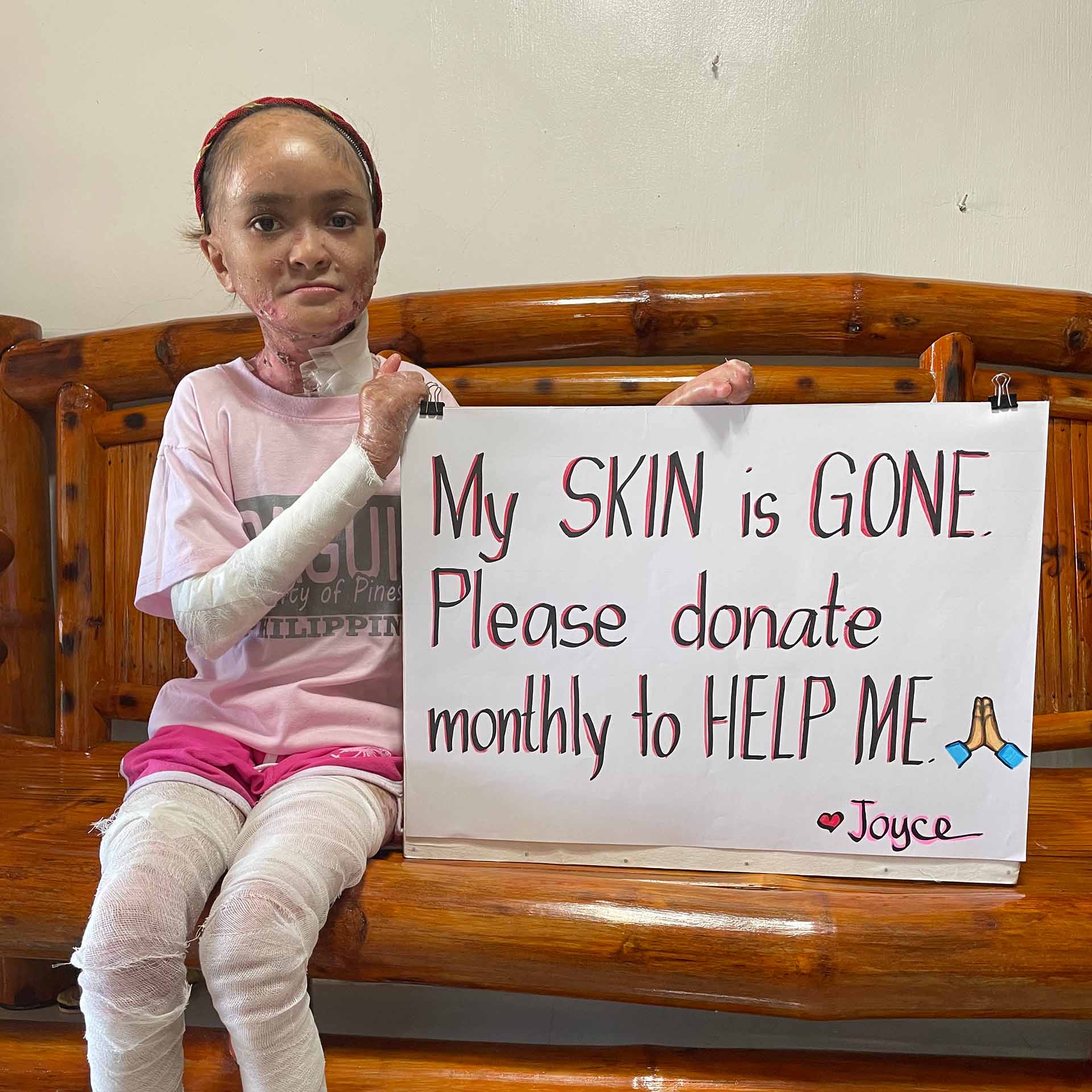 Joyce holding a sign asking for monthly help